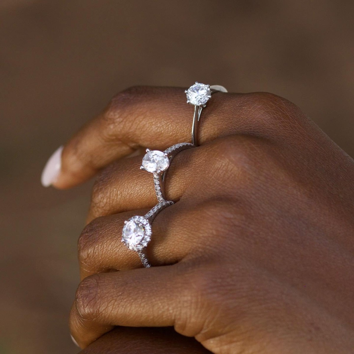 Main portant trois bagues en diamant de synthèse aux montures variées, illustrant le choix d’une bague selon la forme des doigts - Laveran Paris